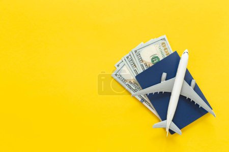 Airplane, passport and dollar bills on a yellow background isolated, top view. Document and money, tourism, vacation and travel concept. Copy space.