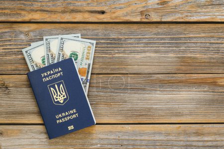 Biometric Ukrainian passport and money on a wooden background isolated. Passport of a citizen of Ukraine and dollar bills close-up. Copy space.
