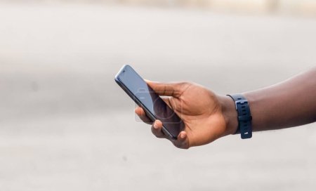 Téléchargez les photos : Main de jeune homme noir africain tenant un smartphone à écran blanc - en image libre de droit