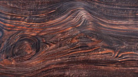 Diese Weitwinkelaufnahme fängt die faszinierenden Muster dunkler Holzmaserung mit hypnotischen Verwirbelungen und lebendigen Kontrast-Highlights ein..