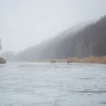 Fog and thaw on a frozen winter river. In the distance a group of people on the ice - fishermen