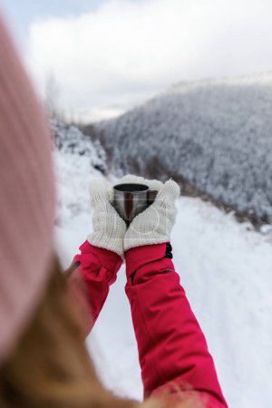 Traveler woman holding cup of coffee on the background of the mountains. Adventure, travel, winter concept.