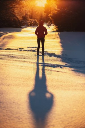 Téléchargez les photos : Young female standing on the snow and enjoying the sunset in the forest - en image libre de droit