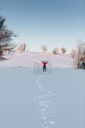 Foto de Joyful woman having fun outdoors in winter. Raised up hands on the mountain covered with snow, enjoying beautiful sunset - Imagen libre de derechos