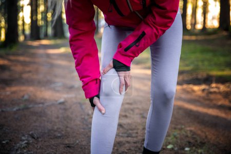 Téléchargez les photos : Injury from workout concept - Caucasian woman use hands hold on her painful knee while running in forest training - en image libre de droit