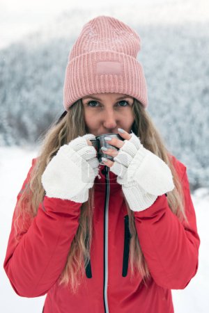Foto de Young woman wearing winter clothing is enjoying hot tea from mug outdoors. Travel concept. Keeping warm in cold weather - Imagen libre de derechos