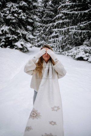 Foto de Portrait of a young stylish caucasian woman posing in park hiding behind a scarf in winter in a wool sweatshirt under a snowfall. Winter walking concept. - Imagen libre de derechos