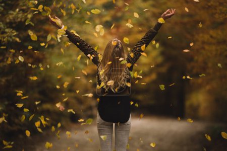Photo for Beautiful woman cheerfully throws autumn leaves in nature - Royalty Free Image