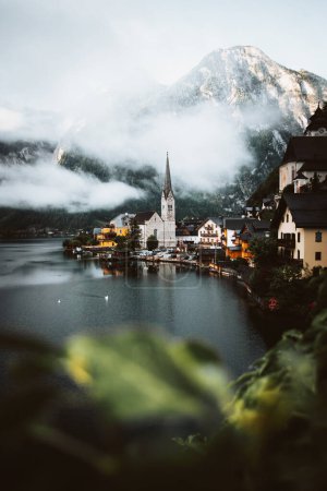 Téléchargez les photos : Moody view of famous beautiful old town Hallstatt and alpine deep lake in scenic foggy morning. Summer season, creative, vintage style - en image libre de droit