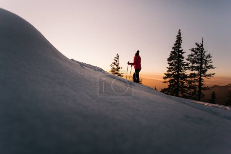 Téléchargez les photos : Hiker woman with walking poles enjoying the majestic sunset during winter at Hasmas mountains, Transylvania, Romania. Outdoor, Adventure concept - en image libre de droit