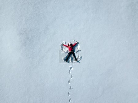 Foto de Aerial shot of woman in snow making snow angel. Woman lying in snow. copy space text. - Imagen libre de derechos