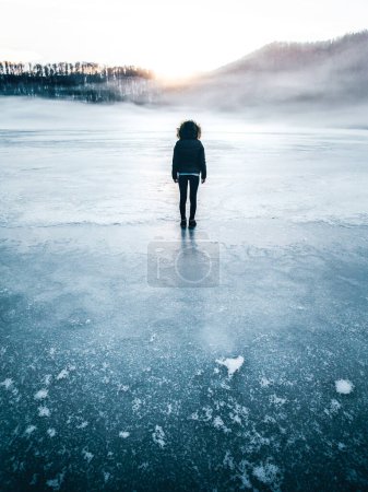 Foto de Woman in the mist walking on the lake ice in winter afternoon. Sunset concept - Imagen libre de derechos