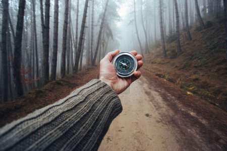 Téléchargez les photos : Male hand with compass on background of road in the forest, point of view. - en image libre de droit