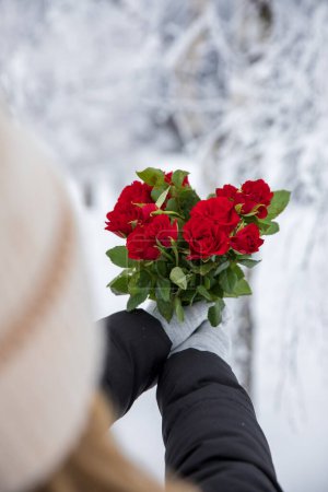 Woman's hand holding a bouquet of red roses in the snowy forest. Valentine's Day Concept.