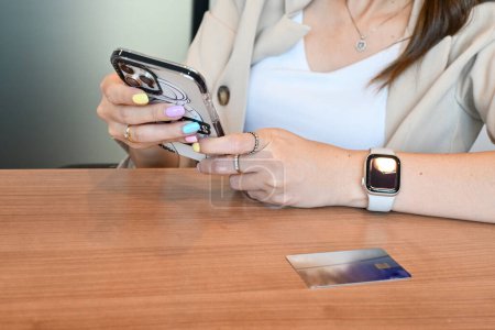 Hands holding smartphone, credit card on table, involved in online mobile shopping at home, happy female shopper purchasing goods or services in internet store. Internet banking, online transactions.