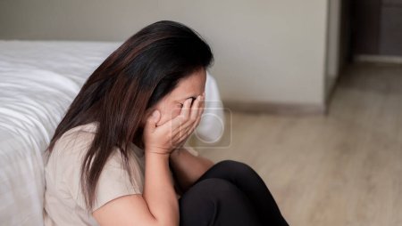 Traurig depressive Asiatin leidet auf dem weißen Bett, sie sitzt im Bett und berührt ihre Stirn, Schlafstörung und Stresskonzept
