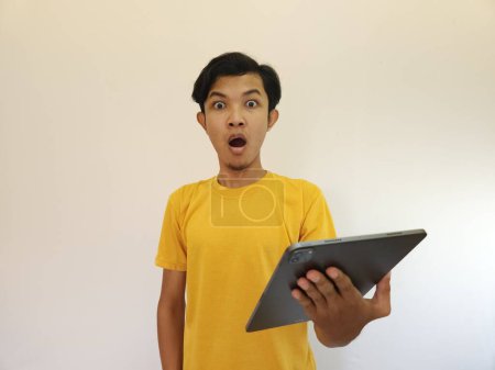 Téléchargez les photos : Incroyable heureux homme asiatique en utilisant tablette numérique en regardant les nouvelles des médias sociaux, choqué homme consommateur surpris excité par la victoire en ligne isolé - en image libre de droit