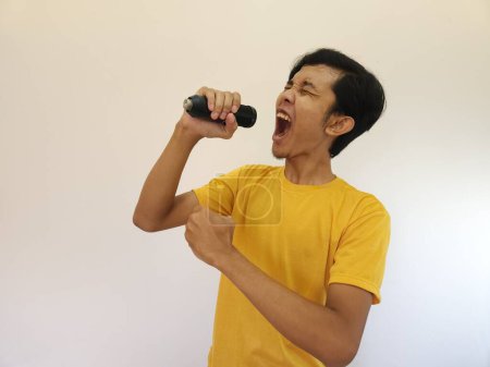 Téléchargez les photos : Portrait de jeune homme asiatique beau chantant une chanson avec un microphone. heureux et se détendre, profiter du moment - en image libre de droit