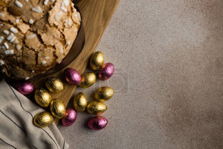 Foto de Pastel de Pascua o pan kulich con almendras y azúcar con chocolate Huevos de Pascua en tabla de cortar de madera, servilleta rayada. Feliz Pascua concepto de vacaciones, receta, espacio de copia - Imagen libre de derechos