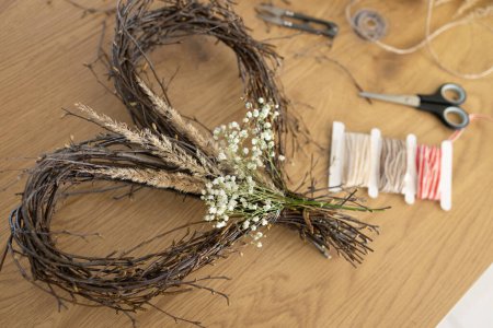 Wicker heart shaped wreath of birch branches and supplies for DIY making on wooden table background. Wreath weaving, crafting, handmade decoration