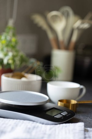 Téléchargez les photos : Balances, bol, cuillère à mesurer, serviette, tasse sur le comptoir de cuisine en béton. Espace vide pour le produit. Concept de cuisson, pesage des ingrédients pour la cuisson, la fabrication et l'alimentation du levain à la maison - en image libre de droit