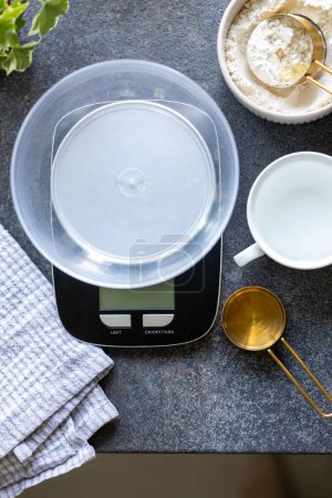 Scales, measuring spoon, napkin, water and flour on concrete kitchen counter. Concept of cooking, weighing ingredients for baking, making and feeding sourdough starter at home. Top view