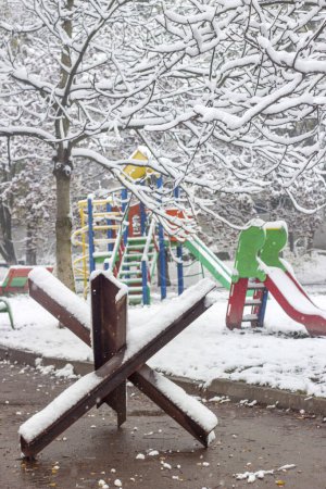 Téléchargez les photos : War in Ukraine. Photo of an anti-tank hedgehog covered in snow on a playground in a residential yard. Stolen childhood from Ukraine. vertical - en image libre de droit