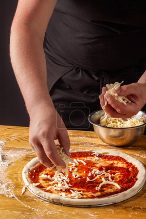 Photo for The process of making pizza. Pizzaiolo tops the dough with grated mozzarella cheese. Vertical. Dark background. - Royalty Free Image