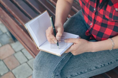 Téléchargez les photos : Jeune femme prenant des notes dans un carnet dans le parc - en image libre de droit