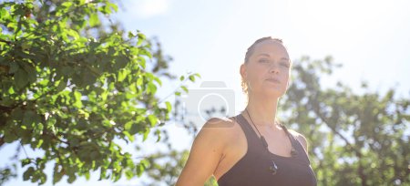 Photo for Sport woman sportswear and headphones training outside in green park looking at camera, banner, copy space for design. - Royalty Free Image