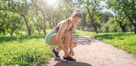 Photo for Sport woman sportswear and headphones tie laces while training jogging running outside in green park banner, copy space for design. - Royalty Free Image