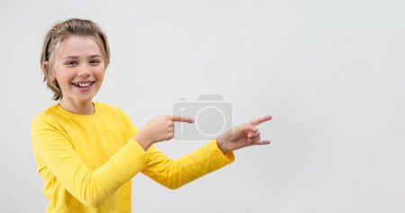 Amazed Emotional School boy happily Joy Showing To Right Over White Background. Copy Space For Advertisement. Excited Blond Kid With Long Hair And Yellow T-Shirt