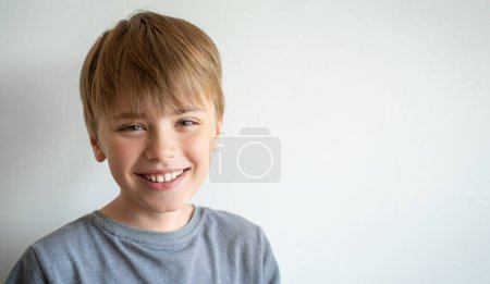 Téléchargez les photos : Portrait d'enfant souriant, adolescent en t-shirt gris regardant la caméra sur fond blanc. Humeur positive. - en image libre de droit
