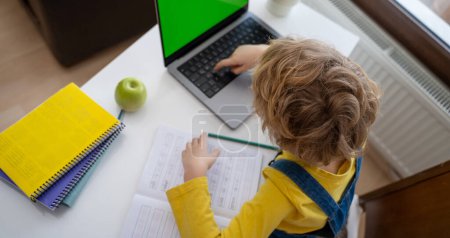 Photo for Caucasian smiling child schoolboy or girl studying at home using laptop remote education. Doing homework, writing exercise book. Copy space. Top view - Royalty Free Image