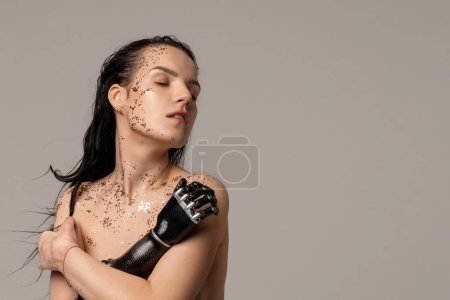 Téléchargez les photos : Femme mince handicapée avec bras prothétique, main artificielle avec paillettes fraîche maquillage nu sur fond beige. Femmes Beauté Diversité. Positif. Espace de copie - en image libre de droit