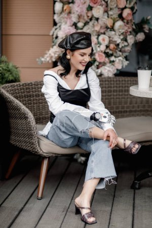 Foto de Beauty disabled french styled Woman with bionic prosthetic arm, artificial hand drink coffee outside in spring flower interior cafe. Vertical. Women diversity Vertical - Imagen libre de derechos