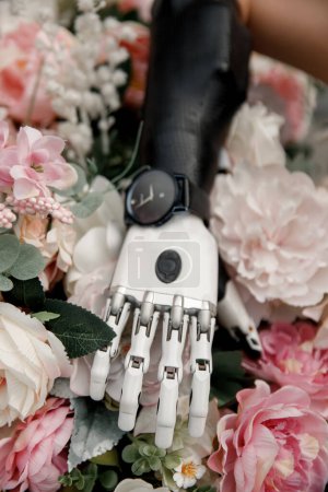 Téléchargez les photos : Bionic artificial hand prosthetic over pink flowers. Vertical selective soft focus. Concept of diversity and possibilities. - en image libre de droit