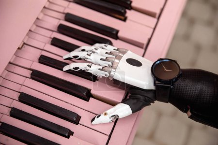 Foto de Bionic artificial hand prosthetic arm playing pink piano. Negative space. Concept of diversity and possibilities. - Imagen libre de derechos
