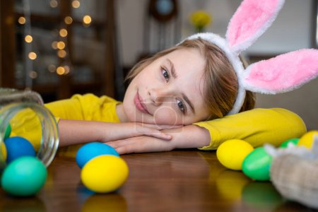 Foto de Easter Family traditions. Close-up caucasian child bunny ears playing with decorated multi-colored eggs. Kid having fun looking at camera. Negative copy space - Imagen libre de derechos