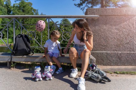 Téléchargez les photos : Maman enfilant des patins à roues alignées pour fille enfant dans le parc public en été. Loisirs en famille jeu d'activité sportive de plein air. - en image libre de droit