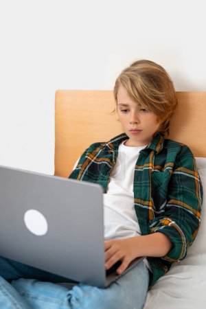 Téléchargez les photos : Smart caucasien collège écolier garçon en utilisant un ordinateur portable. Enfant tapant sur le clavier. Jouez à un jeu vidéo.Tuteur en ligne enseignant classe numérique, leçon web sur ordinateur à la maison. L'éducation virtuelle. Éducation en ligne - en image libre de droit