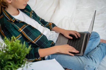 Photo for Teenage child boy using laptop. Child typing on the keyboard lying in bed. Play video game. Schoolboy studying doing homework. E-learning, remote educational classes - Royalty Free Image