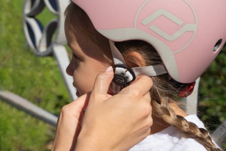 Photo for Mom putting on inline skates rollers protection helmet to daughter child in public park in summer. Family leisure outdoor sport activity game. - Royalty Free Image