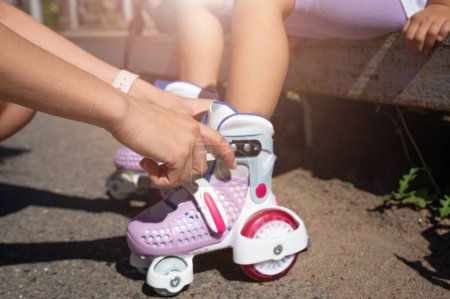 Téléchargez les photos : Gros plan Maman enfilant des patins à roues alignées à sa fille enfant dans un parc public en été. Loisirs en famille jeu d'activité sportive de plein air. - en image libre de droit