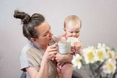 Photo for Family mother and cute baby eating breakfast at home child drinking from mothers cup. Infant tasting solid food, adults meal. First steps Copy space - Royalty Free Image