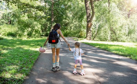Photo for Mother teaching child daughter to skate on inline skates rollers in public park in summer. Family leisure outdoor sport activity game. Copy negative space - Royalty Free Image