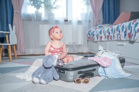 Téléchargez les photos : Bébé fille caucasienne en valise de voyage. Enfant à l'intérieur des bagages emballés pour des vacances pleines de vêtements, d'enfants et de préparation de voyage en famille - en image libre de droit