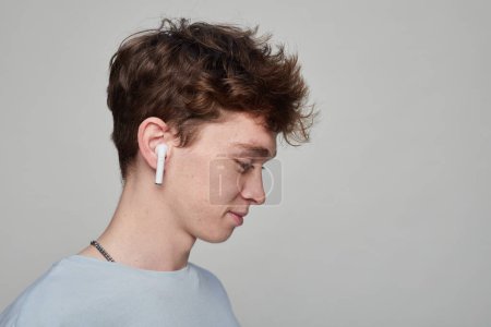 Foto de Vista lateral de un joven que se pone auriculares en un estudio fotográfico con un fondo gris - Imagen libre de derechos