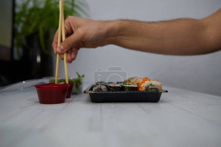 Foto de Vista lateral de la persona anónima de la cosecha comiendo sushi delicioso con palillos mientras está sentado en la mesa en la oficina - Imagen libre de derechos