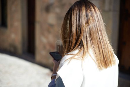 Foto de Anonymous girl on her back using smartphone while walking around town - Imagen libre de derechos